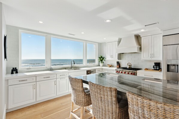 A modern kitchen with a large island, white cabinetry, and a view of the ocean.