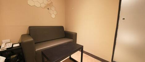 A room with a grey sofa, a small black table, and a wall-mounted hexagonal light fixture.