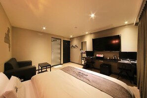 Habitación de hotel con cama, escritorio, silla, televisión y minibar.