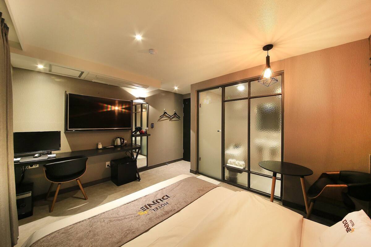 A hotel room with a bed, desk, chair, TV, and a sliding door.