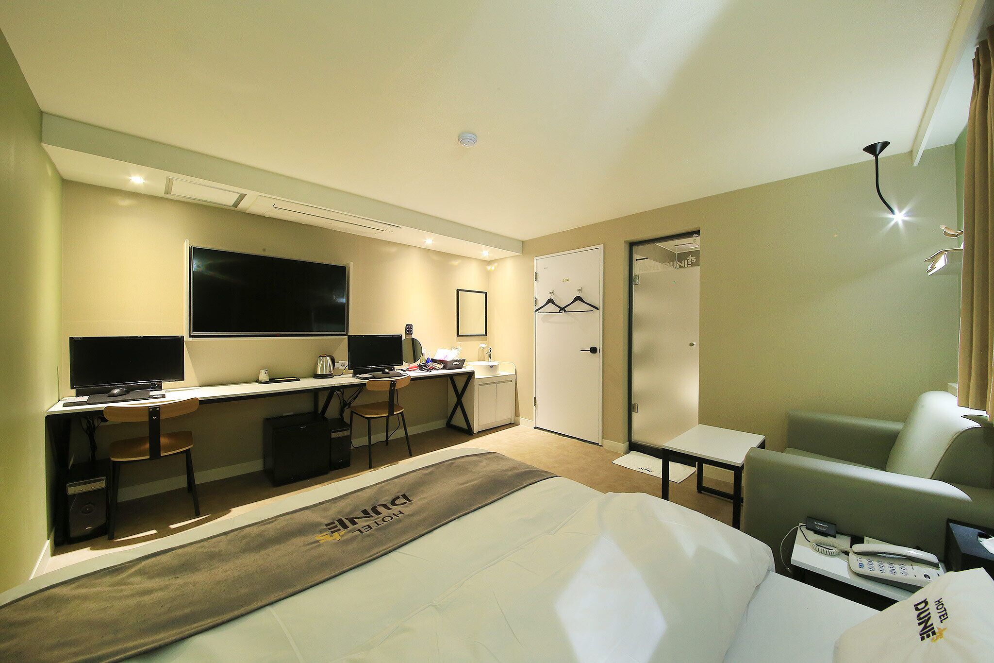 A hotel room with a bed, a desk with a computer, a TV, and a seating area.