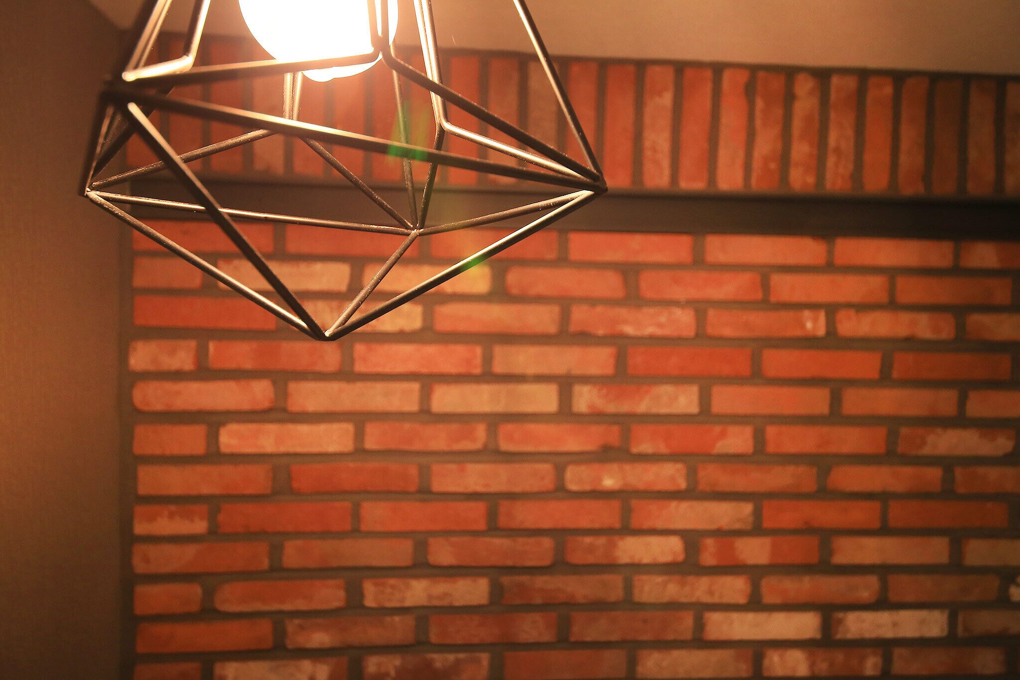 A geometric metal light fixture against a brick wall.