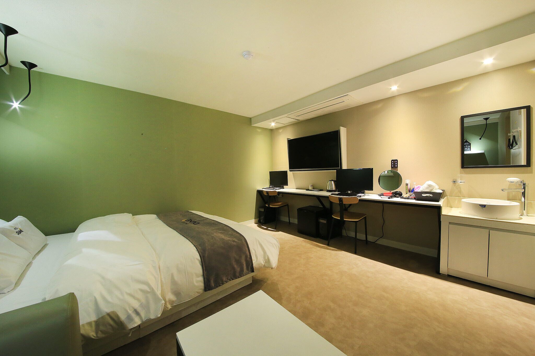 A hotel room with a bed, desk, and a bathroom with a sink and mirror.