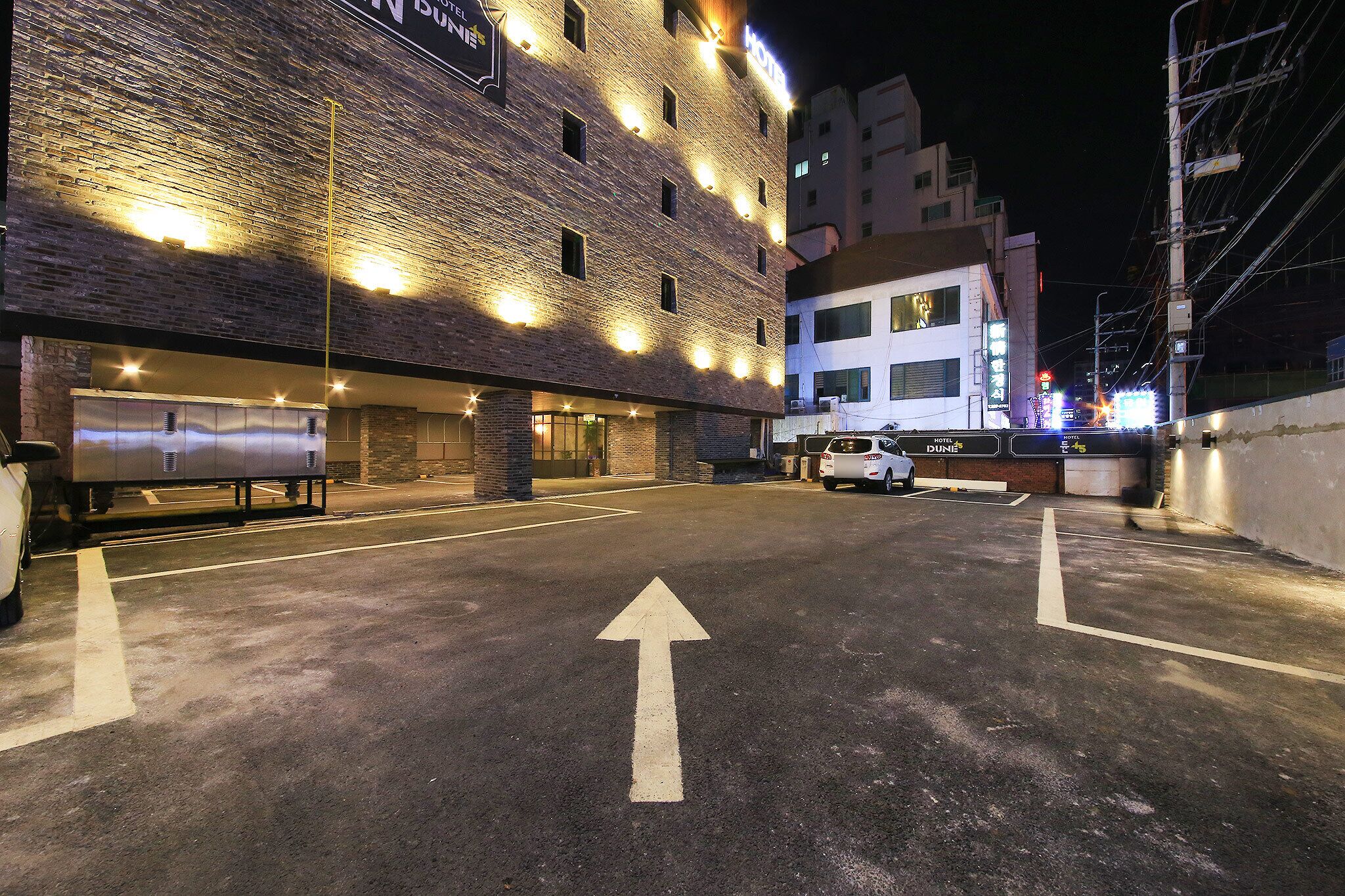 A hotel entrance with a brick facade, illuminated windows, and a clear directional arrow on the ground.