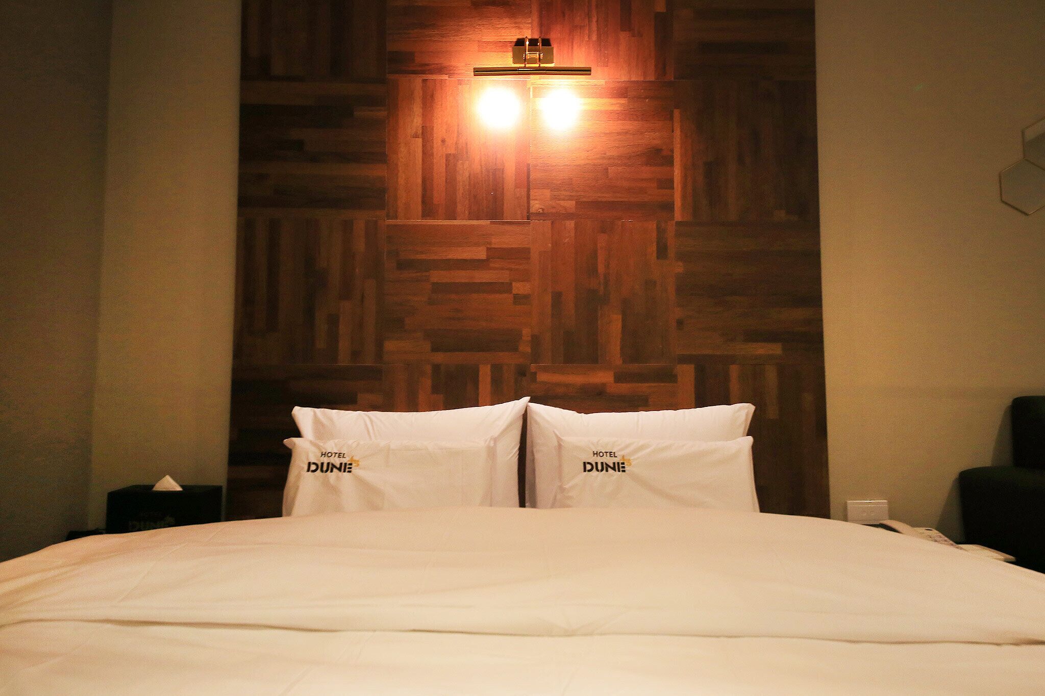 A hotel room with a wooden headboard, two bedside lamps, and pillows with the hotel name.
