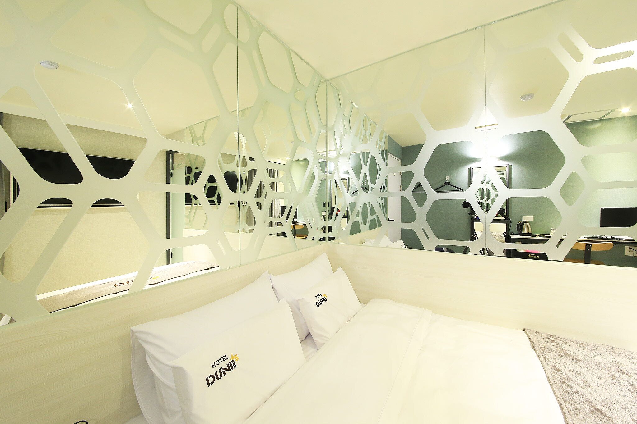 A hotel room with a modern design, featuring a geometric wall partition, a neatly made bed with white linens, and a visible bathroom area with a shower and sink.
