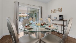 Un comedor con una mesa de vidrio, sillas grises y una barra de café con una máquina de café y un letrero que dice "Coffee Bar".