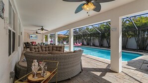 Un espacio al aire libre techado con piscina, muebles de mimbre, ventiladores de techo y una mesa de madera con bebidas.