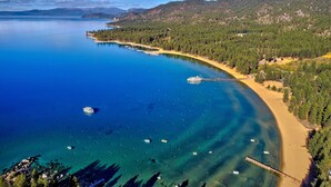 Une zone côtière caractérisée par des eaux bleues et limpides, une plage de sable et une colline boisée.