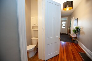 A hallway with a wooden floor, a white door, a white toilet, and a small bench. - The Convent (Cincinnati)