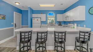 A kitchen with a central island, bar stools, white cabinets, a refrigerator, and a clock on the wall. - Magnolia N 201 (Myrtle Beach)