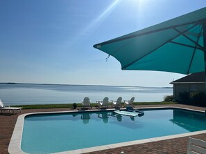 Ein Pool mit Blick auf das Wasser, umgeben von Liegestühlen und einem großen Sonnenschirm.