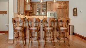 A kitchen with wooden cabinets, a microwave, and four wooden bar stools. - 2 Minute Walk to Cascade Lift + Luxury Penthouse Condo with Covered Parking (Vail)