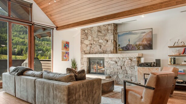 A modern living room with a stone fireplace, a large sofa, and a wooden ceiling. - 2 Minute Walk to Cascade Lift + Luxury Penthouse Condo with Covered Parking (Vail)