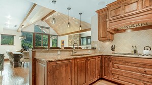 A spacious kitchen with wooden cabinets, a large island, and a stone backsplash. - 2 Minute Walk to Cascade Lift + Luxury Penthouse Condo with Covered Parking (Vail)