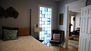 A bedroom with a bed, a chair, a lamp, and a window with blue-tinted glass. - Mermaid Tale-Bohemian Bungalow (Dayton)
