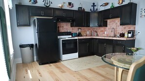 A compact kitchen with dark cabinets, a black refrigerator, a stove, and a microwave. There's a small dining area with a glass table and a chair. - Mermaid Tale-Bohemian Bungalow (Dayton)