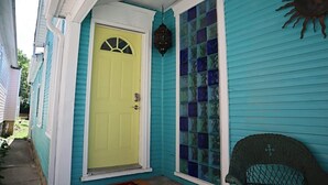 A house with a bright yellow front door, a glass door with a grid pattern, and a wicker chair outside. - Mermaid Tale-Bohemian Bungalow (Dayton)