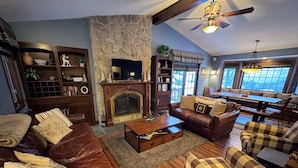 A cozy living room with a fireplace, leather sofas, a coffee table, and a dining area with a large table and chairs. - FC17 Stylishly renovated Forest Cottage, walk to ski trails, wifi, cable, ping pong, AC! (Bretton Woods)