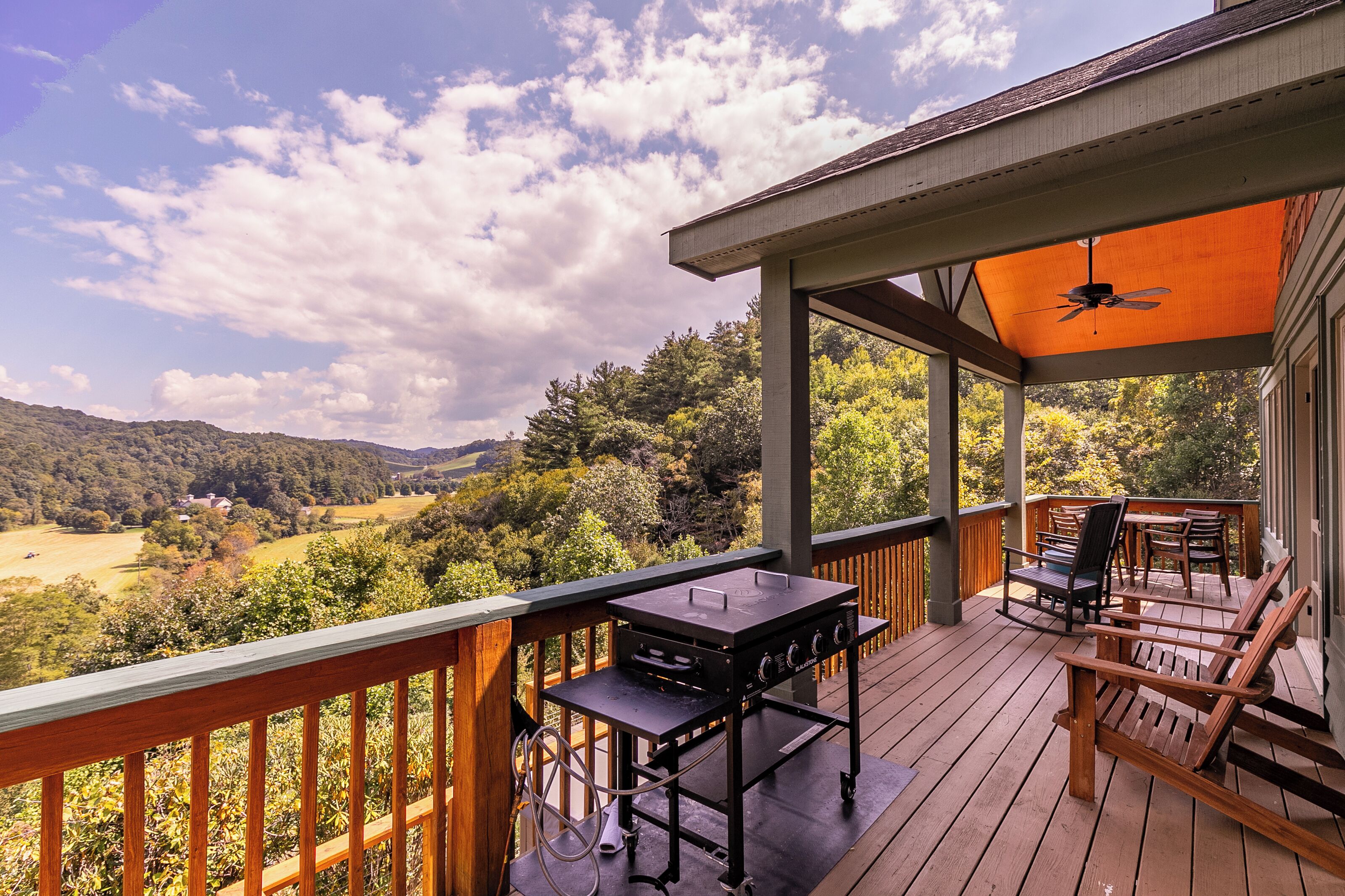 A covered outdoor deck with a grill, chairs, and a scenic view of a valley.