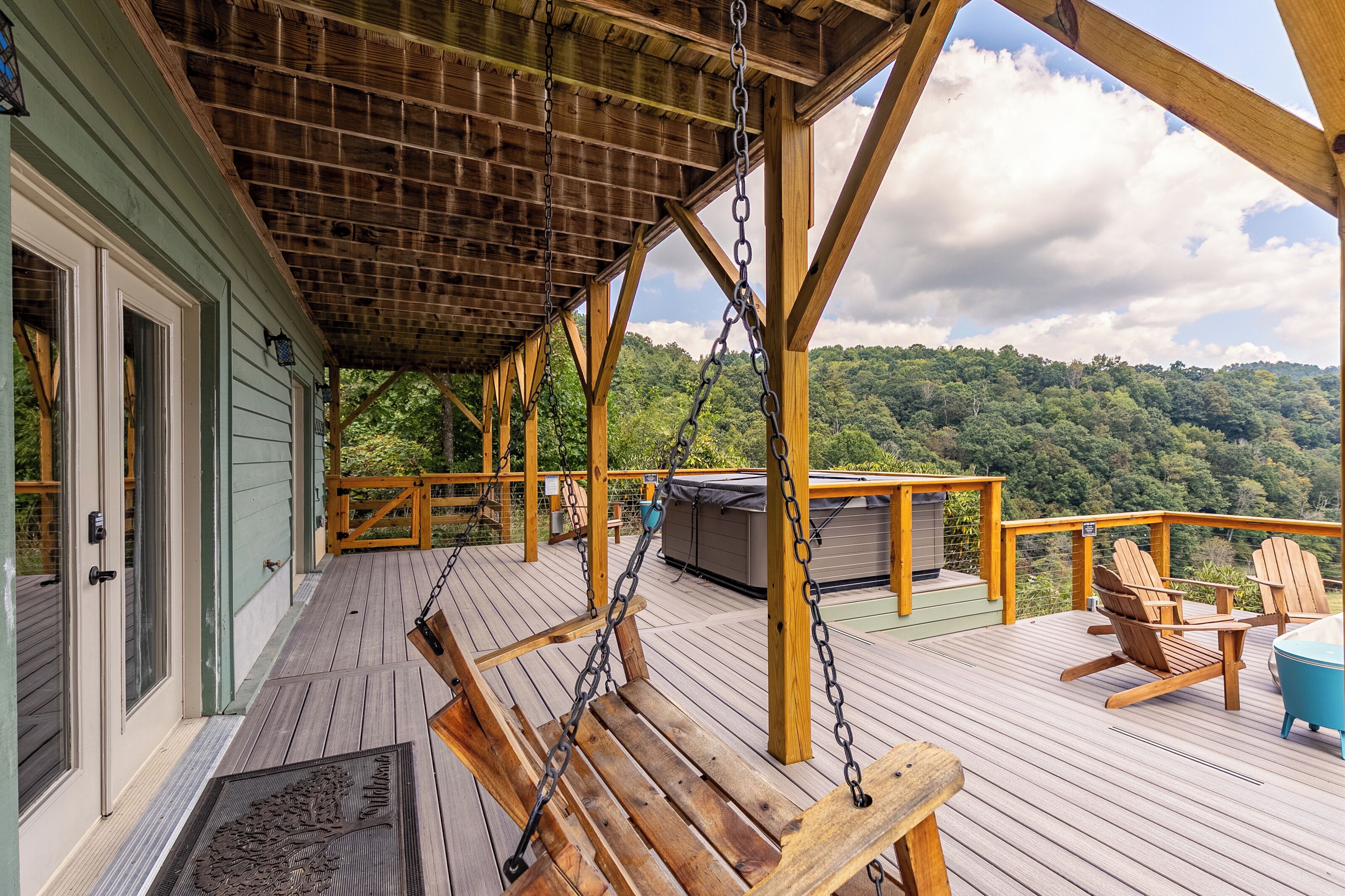A wooden deck with a swing, chairs, and a view of a forested hill.