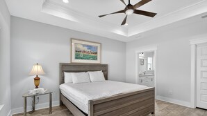 Une chambre à coucher avec un lit en bois, une table de chevet avec une lampe, un ventilateur de plafond et un tableau encadré au mur.
