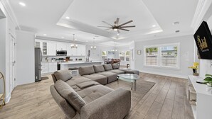 Un vaste espace de vie comprenant un grand canapé d’angle, une table basse en verre et un ventilateur de plafond.