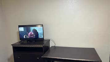 A television on a wooden stand with a dark desk beside it.
