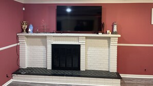 A room with a white brick fireplace, a flat-screen TV mounted above it, and a red wall. - private 6 Bedroom charming  2000 sq ft ranch 10-14 people (Sterling Heights)