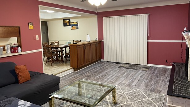 A living room with a glass coffee table, a dark sofa, a ceiling fan, and a kitchen area in the background. - private 6 Bedroom charming  2000 sq ft ranch 10-14 people (Sterling Heights)