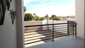 A balcony with a metal railing, a concrete wall, and a view of palm trees and buildings in the distance. - New Town Condo Casamar 2 near the beach (Puerto Peñasco)