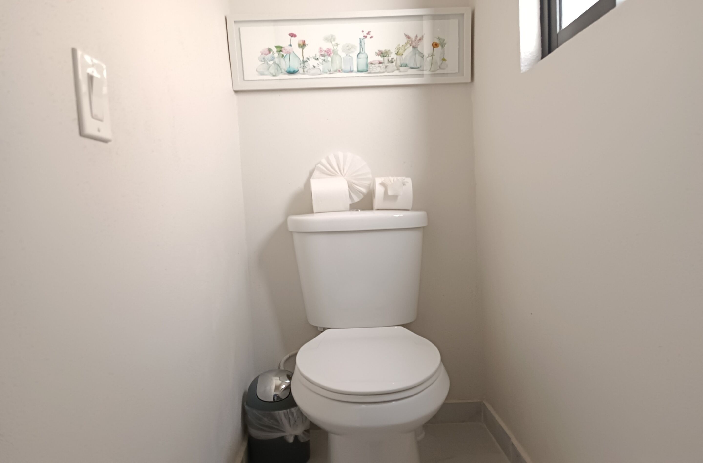 Inodoro blanco con un rollo de papel higiénico y un bote de basura a un lado.