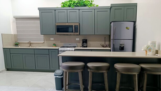 A kitchen with grey cabinets, a microwave, a refrigerator, a stove, and two bar stools. - New Town Condo Casamar 2 near the beach (Puerto Peñasco)