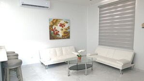A modern living room with a white sofa, a glass coffee table, and a painting on the wall. - New Town Condo Casamar 2 near the beach (Puerto Peñasco)
