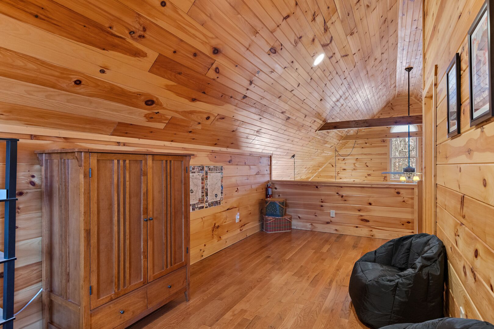 Un intérieur en bois avec un plafond haut, une armoire en bois, une carte accrochée au mur et un pouf noir posé sur le sol.