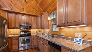 A modern kitchen with wooden cabinets, stainless steel appliances, granite countertops, and a built-in dishwasher. - Cabin with Appalachian Mountain Views (Boone)