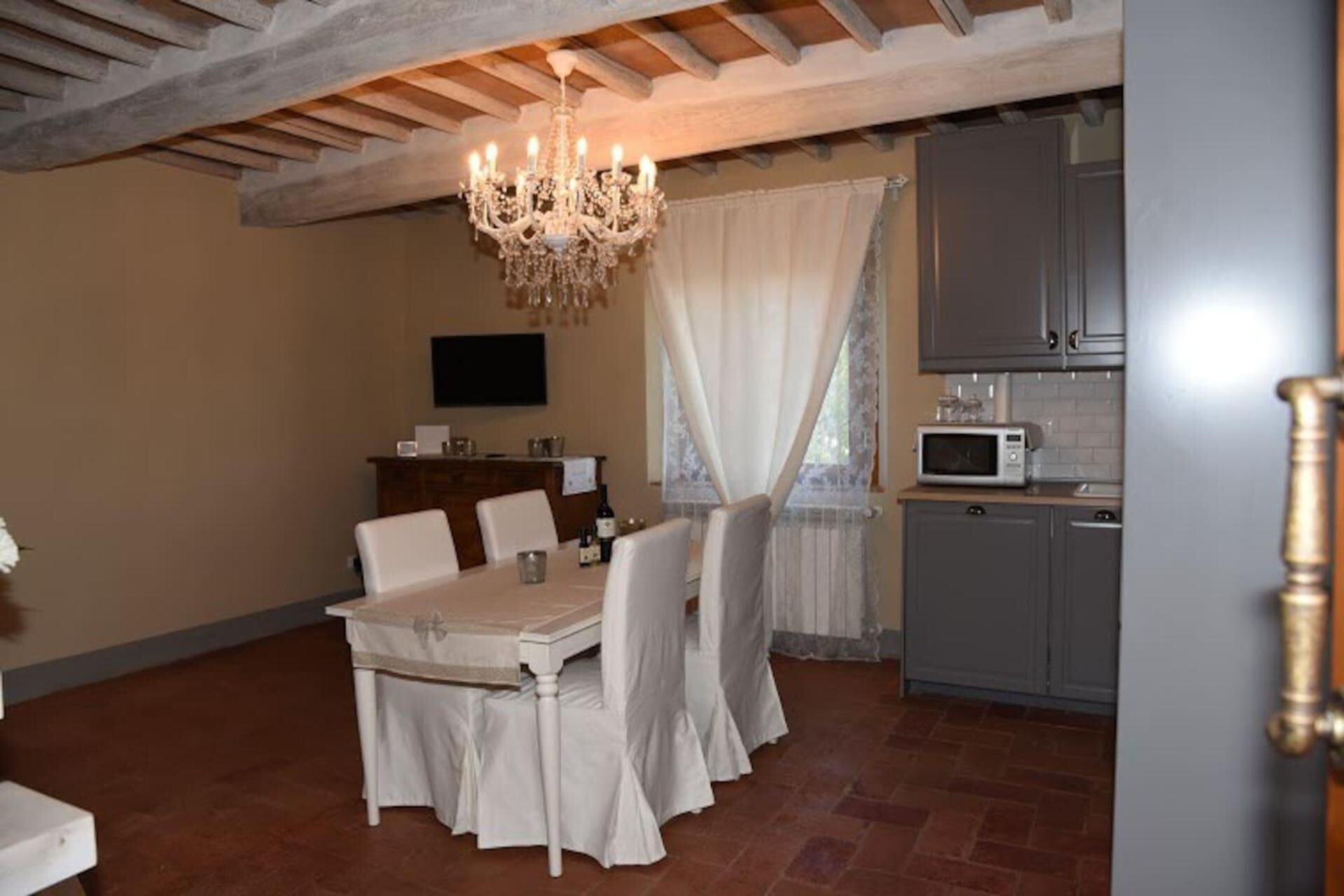 A dining area with a table set for four, a chandelier, and a kitchen with a microwave.