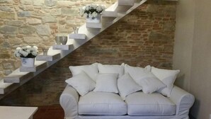 A white sofa with multiple cushions in a room with a stone wall and a wooden staircase. - Beautiful Lux Apartment Chianti Firenze Area Italy (Barberino Tavarnelle)