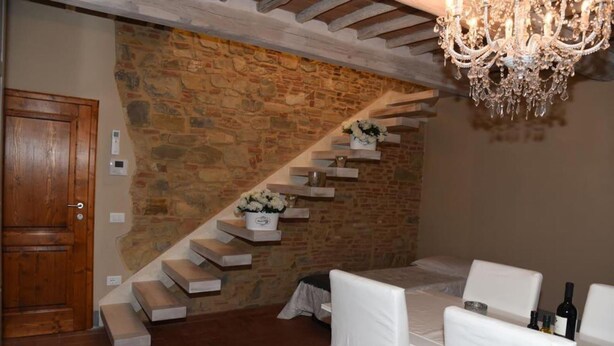A dining area with a stone wall, a wooden staircase, and a chandelier. - Beautiful Lux Apartment Chianti Firenze Area Italy (Barberino Tavarnelle)