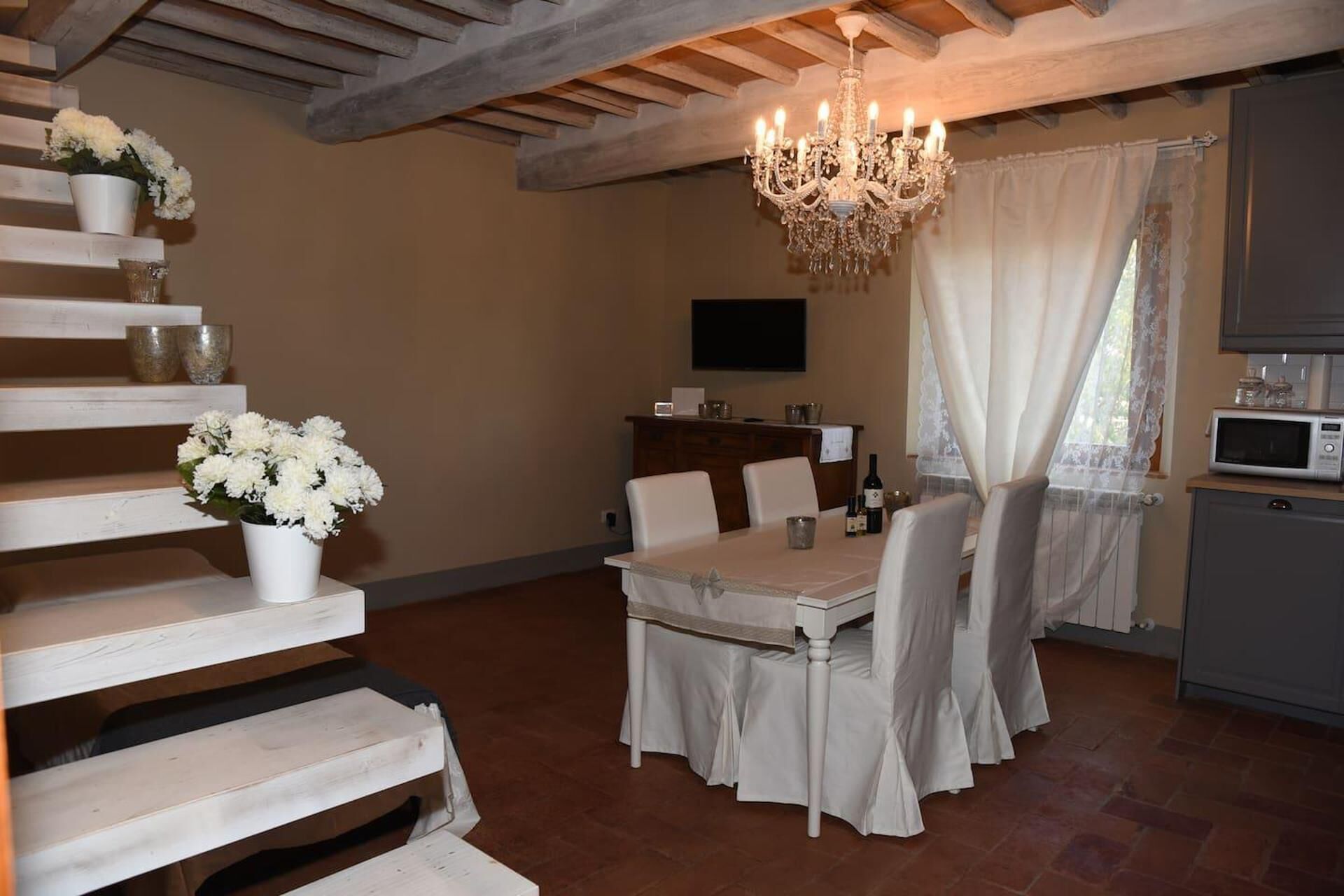A dining area with a table set for four, a chandelier, and a staircase with white steps.