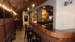 Un espace bar avec un comptoir et des tabourets en bois, un mur en pierre et un coin cuisine à l’arrière-plan.