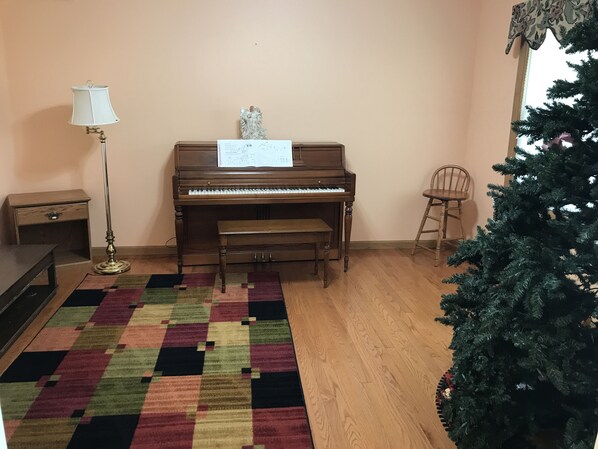 Una habitación con un piano, una pequeña mesa, una silla, una lámpara y un árbol de Navidad.