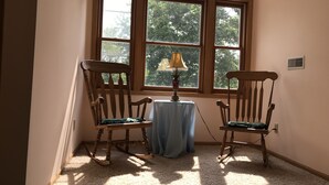 A corner room with two rocking chairs, a table with a lamp, and a large arched window with a view of trees. - Enjoy Florida in Illinois; House on Island with Pool (East Moline)