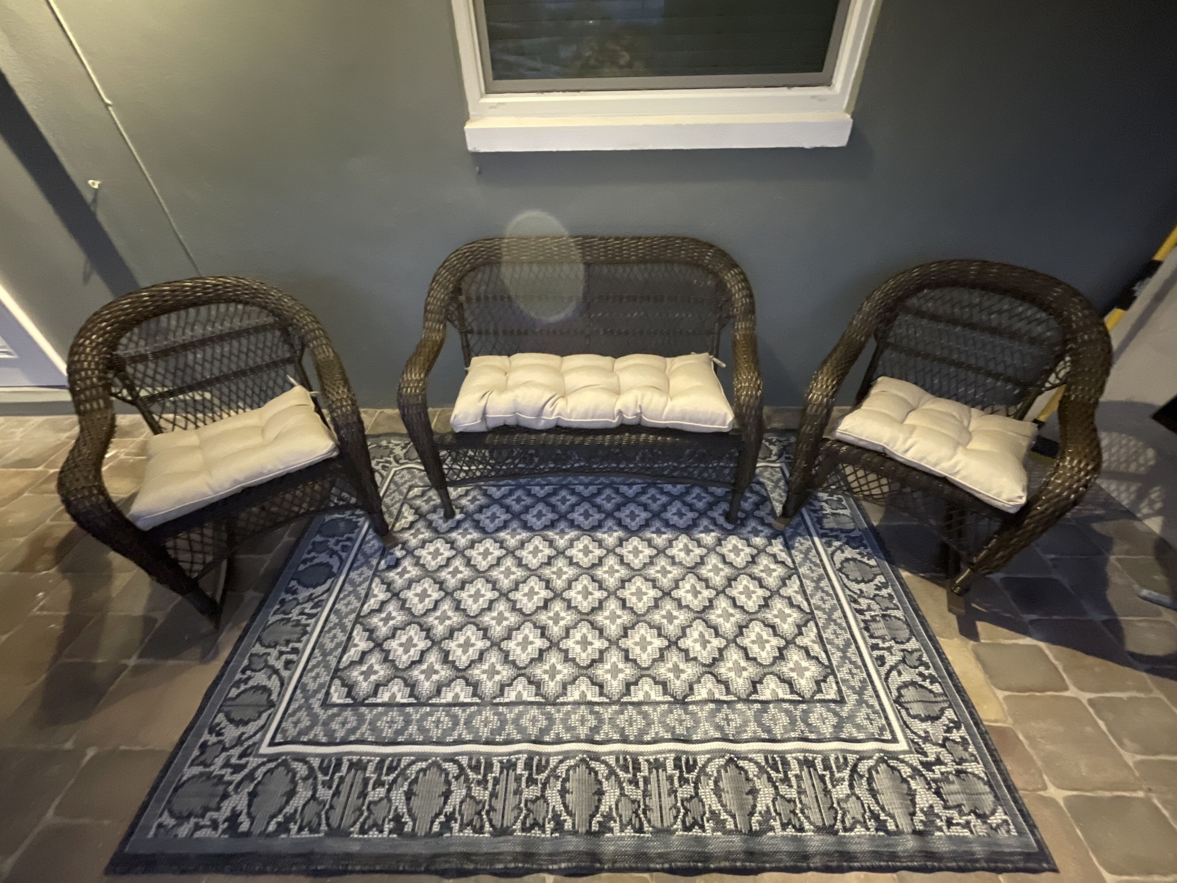 Un rincón con tres sillas de mimbre y una alfombra estampada.