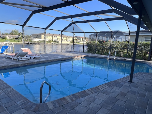 Una piscina con zona cubierta, sillas de descanso y vistas despejadas del barrio circundante.
