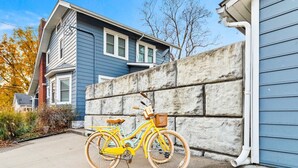 En gul cykel står parkerad framför ett blått hus med en mur av sten.