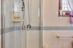 A shower with a glass door, a wooden shelf, and a towel rack.