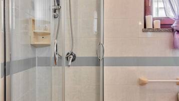 Une douche avec une porte en verre, une étagère en bois et un porte-serviettes.