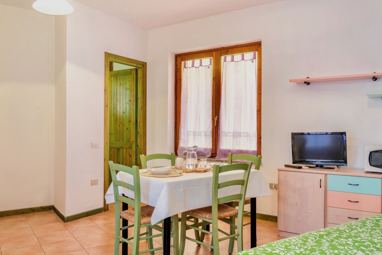 A small, clean room with a dining table set for two, a television, and a cabinet.