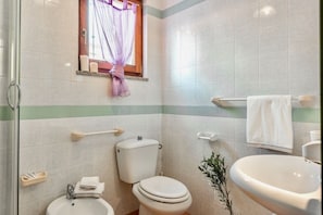A bathroom with a toilet, sink, and window with a curtain.